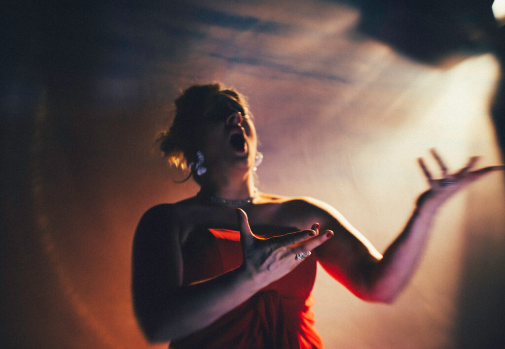 photopraph of opera singer in red dress on stage with lights in background
